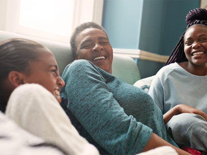 Photo of African American mother and daughters laughing on the couch